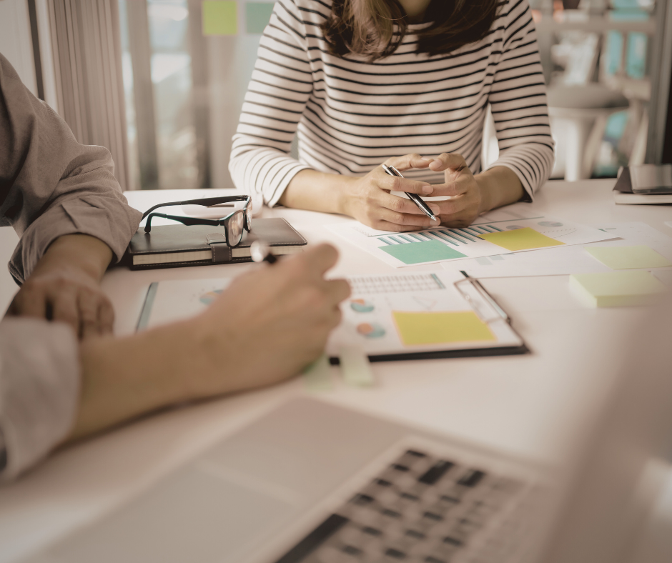 two people working together at a desk with notepads and a laptop